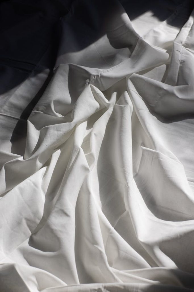 Soft white bed sheets with natural light and shadows creating a serene atmosphere.