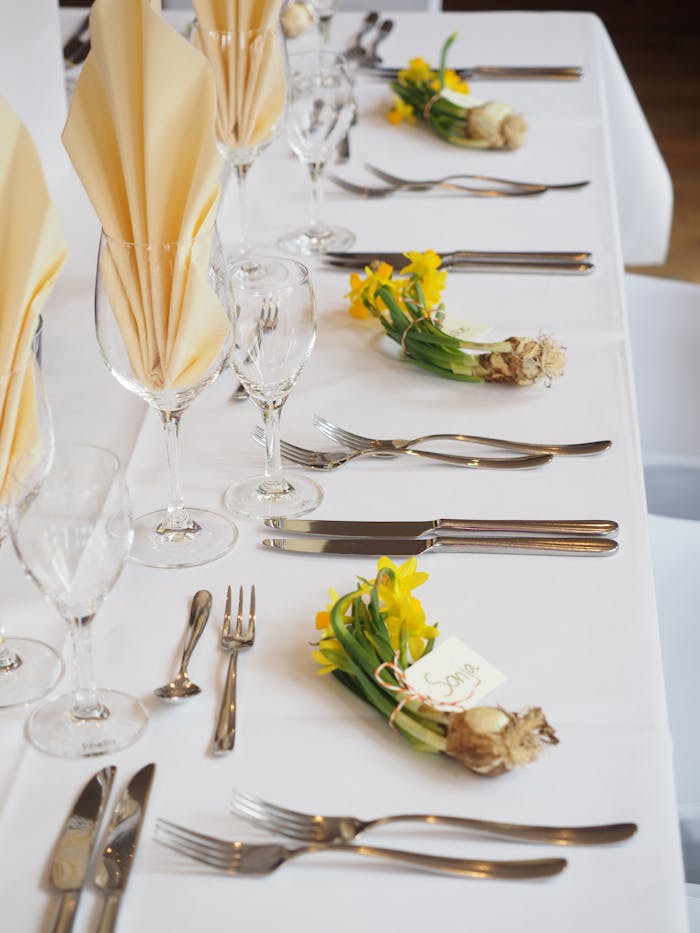 Sophisticated dining arrangement with daffodils and fine cutlery on a white tablecloth.